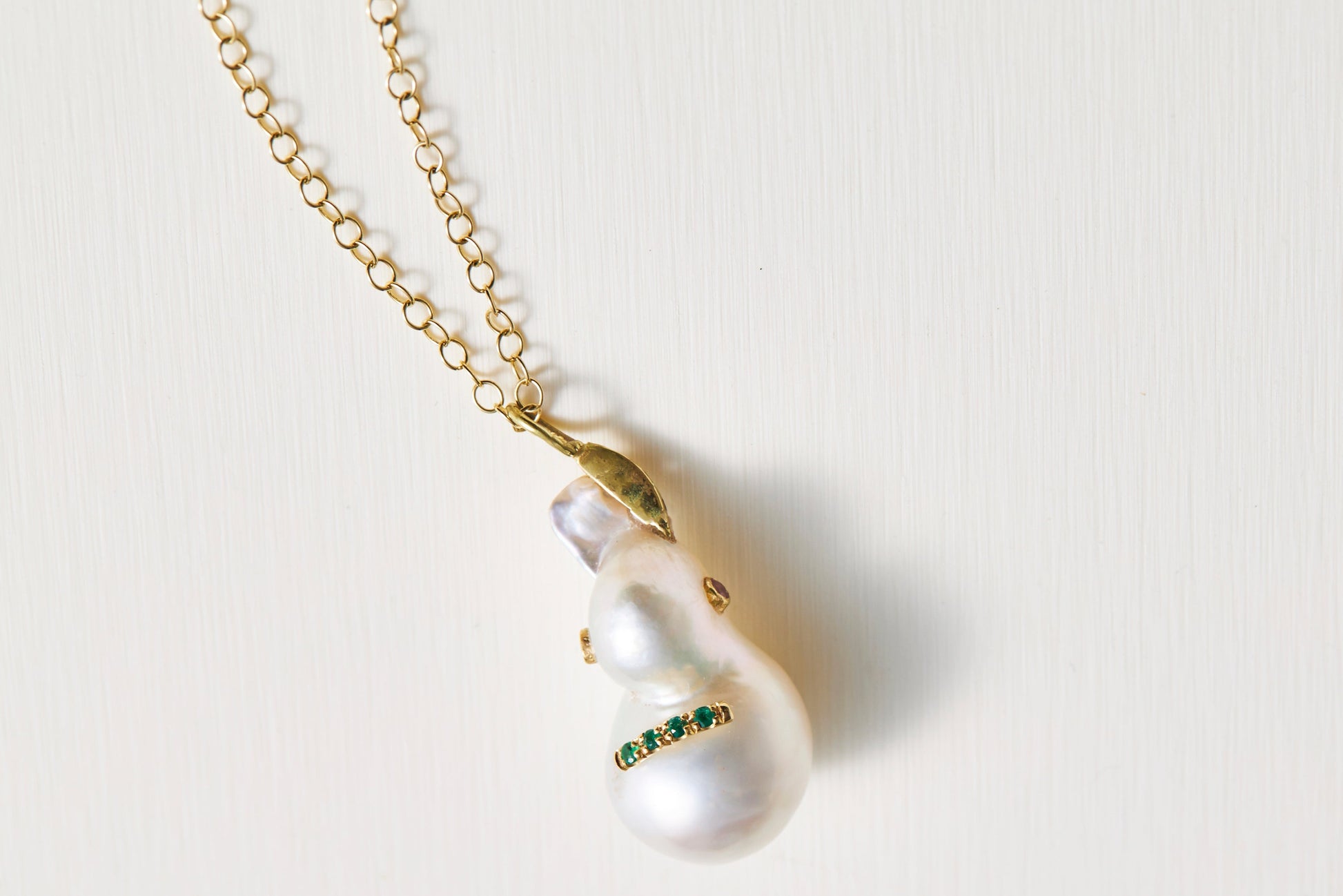 Pearl necklace with gold chain and green gemstones on a light background